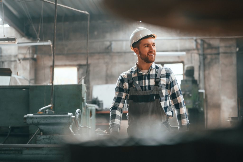 Front view. Factory male worker in uniform is indoors