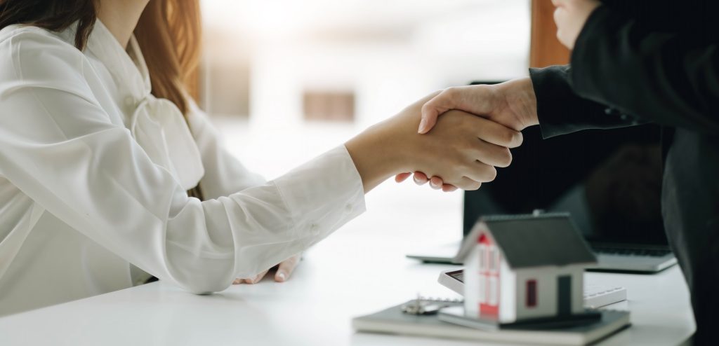 Two business people shaking hands as successful agreement in real estate agency office. Concept of