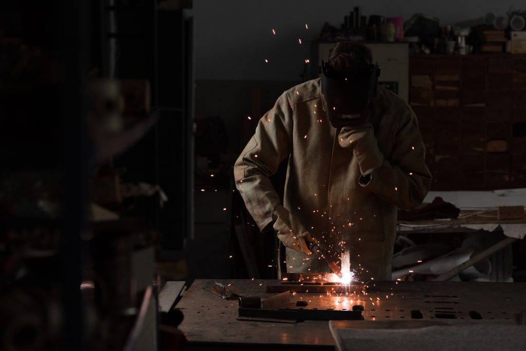 worker in protection mask welding metal at factory